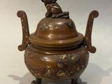 une image représentant un petit pot en bronze surmonté d'un oiseau