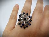 an image of a woman ' s hand holding a ring with blue and white stones