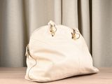 a white handbag sitting on a table with a curtain behind it