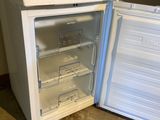 un petit réfrigérateur blanc dont la porte est ouverte, posé à même le sol