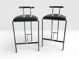 une paire de tabourets de bar en cuir noir avec des pieds et des dossiers en métal