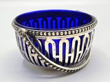 a blue glass bowl with a silver handle on a white surface