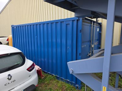 une voiture blanche garée à côté d'un conteneur d'expédition bleu