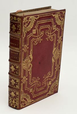 an old red book with gold trim sitting on top of a white surface