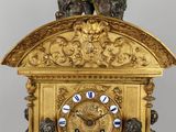 a gold clock with statues around it on a table