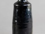 un vase noir surmonté d'un couvercle en bois, posé sur une table