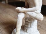 une petite statue représentant un homme assis sur un tabouret