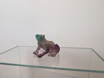 figurine de grenouille violette assise sur une table en verre, coiffée d'une couronne