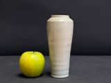 a white vase next to an apple on a table