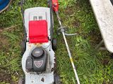 une tondeuse à gazon posée sur l'herbe, à côté d'une poubelle