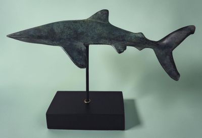 statue d'un requin posée sur un socle noir, sur fond vert