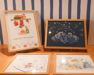 trois photos encadrées posées sur une table en bois, avec en arrière-plan un mur rayé de bleu et de blanc