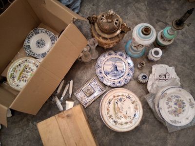 une boîte remplie d'assiettes en porcelaine et d'autres objets, posée par terre