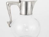 un pichet en verre transparent muni d'une poignée en métal, posé sur une surface blanche