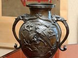 a bronze vase sitting on a glass table in a room