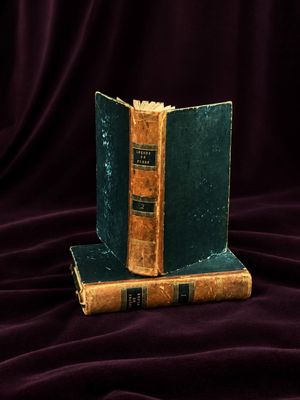 two books sitting on top of each other on a purple cloth