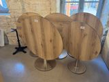 trois tables rondes en bois sur des socles, dans une pièce