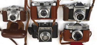 several cameras are lined up on a white surface with a brown strap