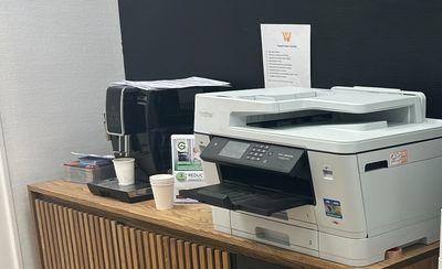 une photo d'une pièce dans laquelle se trouvent un réfrigérateur, une imprimante et d'autres fournitures de bureau