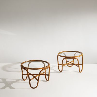 une paire de tabourets en rotin avec un plateau en verre, posés sur un support blanc