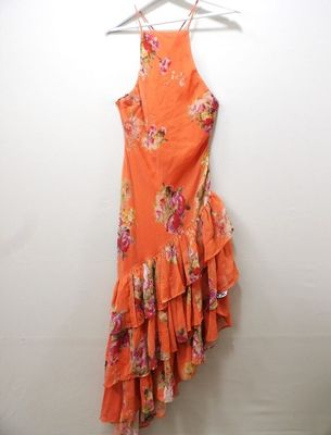 an orange floral dress hangs on a hanger against a white wall
