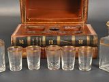 five glass bottles and six glasses in front of a wooden box