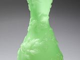 un vase vert posé sur une table, dont l'ombre se projette sur le sol