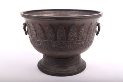 un grand vase en métal posé sur une surface blanche