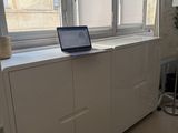a laptop sitting on top of a white cabinet in front of a window