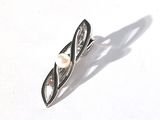 a silver brooch with a pearl in it on a white surface