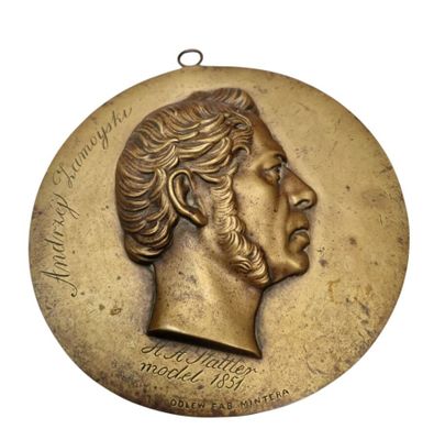 une image représentant un médaillon en bronze orné du visage d'un homme