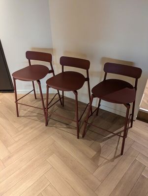 trois tabourets en bois posés sur un parquet, près d'un mur blanc