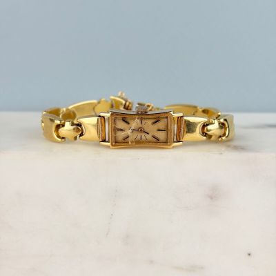 une photo d'une montre en or posée sur une surface en marbre