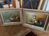 deux tableaux encadrés représentant des fruits et une cruche posés sur une table