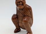 an old wooden figurine of a man squatting on a white surface