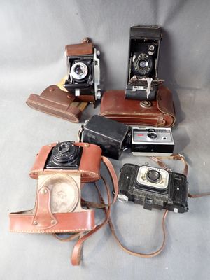 four old cameras sitting on a table with a leather case