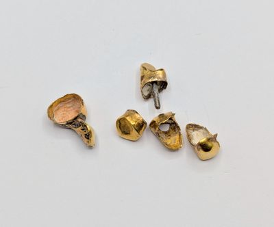 trois pièces de métal doré reposent sur une surface blanche