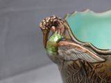 a green vase with a bird on it on a table