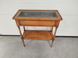 an old wooden table with a glass top and shelf underneath it