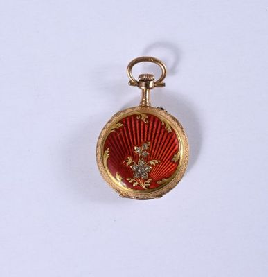 une montre de poche rouge et dorée posée sur une surface blanche