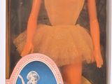 Poupée Barbie ballerine dans sa boîte, posée sur une surface blanche avec un fond rose