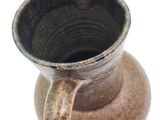 a brown vase with a handle sitting on a white surface