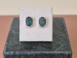 une paire de boucles d'oreilles à clous ornées d'émeraudes, posée sur un bloc de marbre