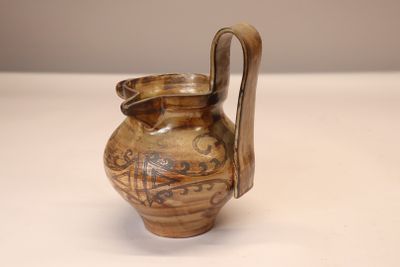 un vase marron muni d'une anse, posé sur une table blanche