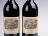 two bottles of red wine sitting next to each other on a white surface