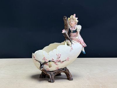 une petite figurine représentant une petite fille assise sur une coquille d'œuf