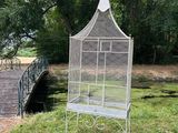 a white bird cage sitting on the grass near a bridge