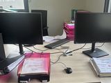 two computer monitors sitting on a desk in front of a window