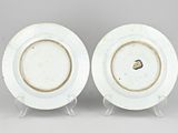two white plates with gold rims on stands against a gray background