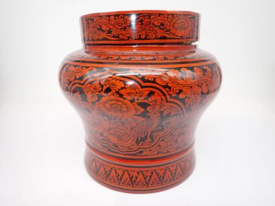un vase rouge et noir posé sur une surface blanche